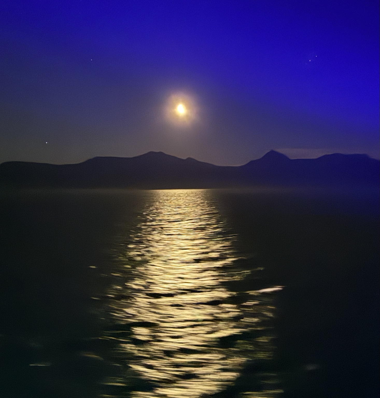 Moonlight reflected on dark water beneath an Alaska mountain silhouette